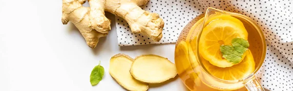 Vue du dessus du thé chaud sur serviette près de la racine de gingembre, citron et menthe sur fond blanc, vue panoramique — Photo de stock