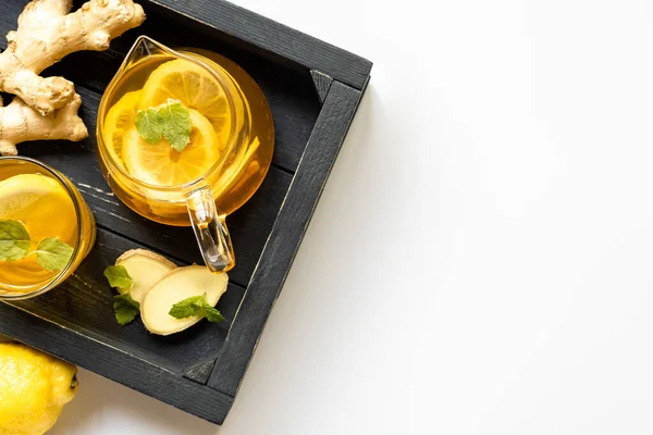 Vue du dessus du thé chaud avec racine de gingembre, citron et menthe sur plateau en bois sur fond blanc — Photo de stock