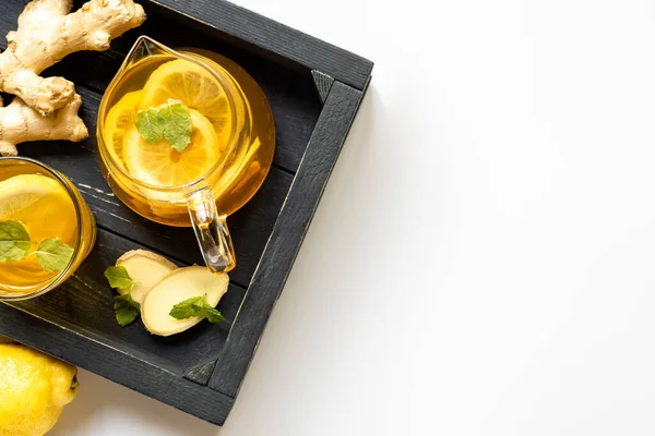 Top view of hot tea with ginger root, lemon and mint on wooden tray on white background — Stock Photo