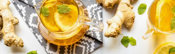 Draufsicht auf heißen Tee auf Serviette in der Nähe von Ingwerwurzel, Zitrone und Minze auf weißem Hintergrund, Panoramaaufnahme — Stockfoto