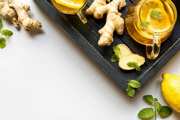 Vista superior de té caliente con raíz de jengibre, limón y menta en bandeja de madera sobre fondo blanco - foto de stock