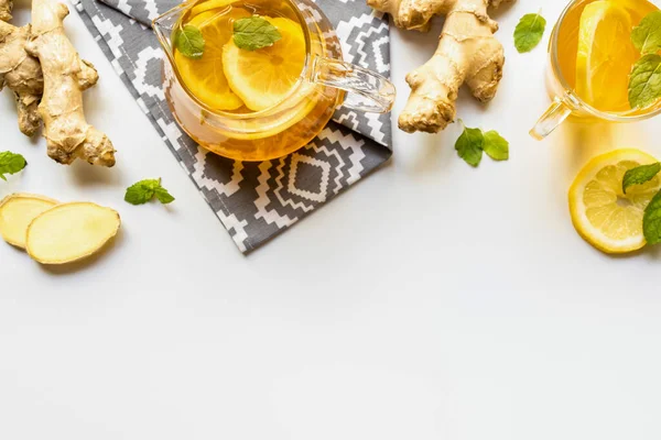 Vue du dessus du thé chaud sur serviette près de la racine de gingembre, citron et menthe sur fond blanc — Stock Photo