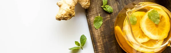 Vue du dessus du thé chaud avec citron près de la racine de gingembre et menthe sur planche à découper en bois sur fond blanc, vue panoramique — Photo de stock