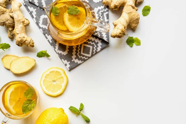 Vue du dessus du thé chaud sur serviette près de la racine de gingembre, citron et menthe sur fond blanc — Photo de stock