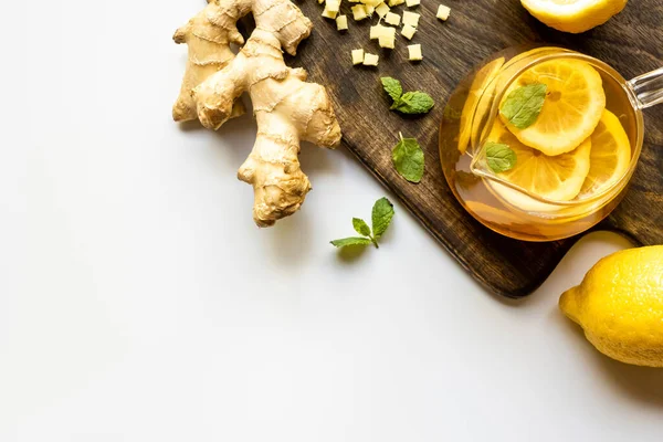 Vue du dessus du thé chaud près de la racine de gingembre, citron et menthe sur planche à découper en bois sur fond blanc — Photo de stock