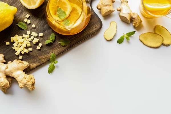 Draufsicht auf heißen Tee in der Nähe von Ingwerwurzel, Zitrone und Minze auf Holzschneidebrett auf weißem Hintergrund — Stockfoto