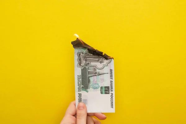 KYIV, UCRANIA - 25 de marzo de 2020: vista recortada de una mujer que sostiene un billete de rublo en llamas aislado en amarillo - foto de stock