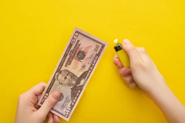 QUIIV, UCRÂNIA - MARÇO 25, 2020: visão recortada da mulher segurando o isqueiro perto da nota de dólar isolada no amarelo — Fotografia de Stock
