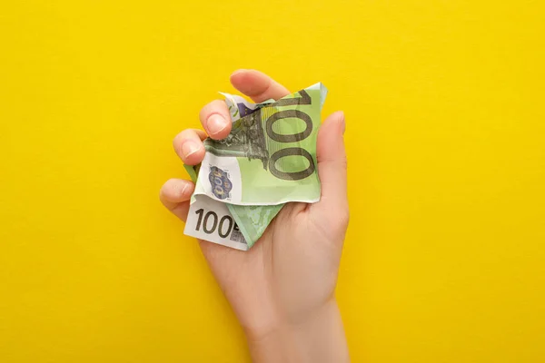 Обрезанный вид женщины, держащей скомканную банкноту евро изолированной на желтом — стоковое фото