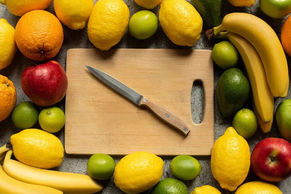 Top view of tasty colorful fruits and wooden cutting board with knife — Stock Photo