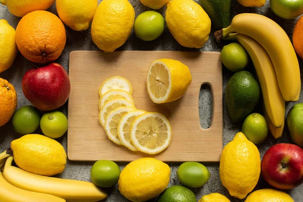 Вид зверху смачні барвисті фрукти і дерев'яна обробна дошка зі скибочками лимона — стокове фото