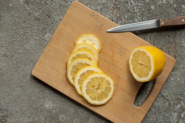 Zitronenscheiben auf Holzschneidebrett mit Messer auf grauer Betonoberfläche — Stockfoto