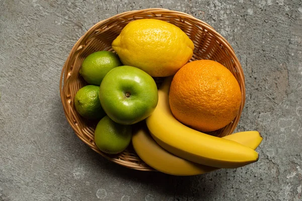 Top view of colorful fresh fruits in wicker basket on grey concrete surface — Stock Photo