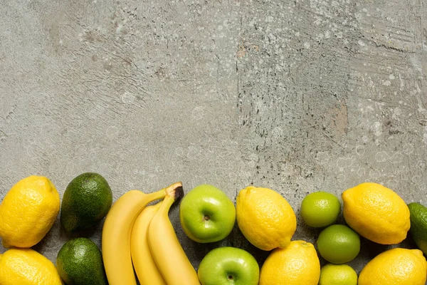 Вид сверху на красочные бананы, яблоки, авокадо, лаймы и лимоны на серой бетонной поверхности — стоковое фото
