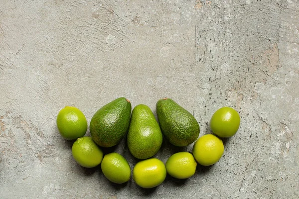 Top view of green avocado, limes on grey concrete surface — Stock Photo