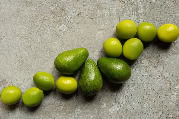 Вид сверху на зеленый авокадо, лаймы на серой бетонной поверхности — стоковое фото