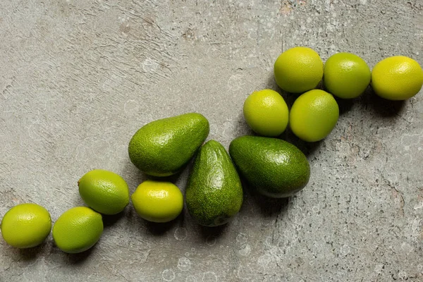 Top view of green avocado, limes on grey concrete surface — Stock Photo