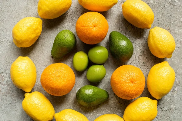 Draufsicht auf bunte Orangen, Avocado, Limetten und Zitronen, die im Kreis auf grauer Betonoberfläche angeordnet sind — Stockfoto