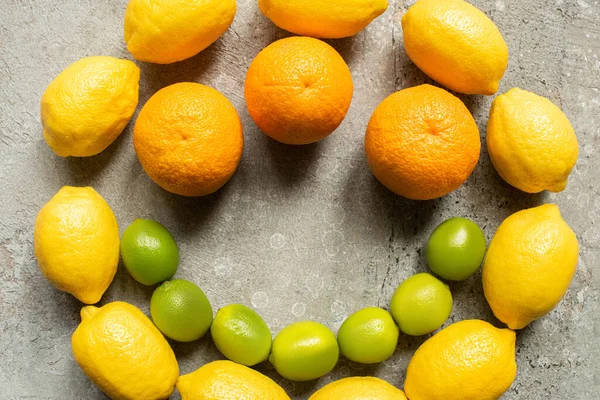 Vista superior de coloridas naranjas, aguacate, limas y limones dispuestos en círculo sobre una superficie de hormigón gris - foto de stock