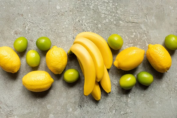 Vista dall'alto di banane, lime e limoni colorati su una superficie di cemento grigio — Foto stock