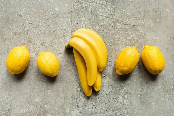 Draufsicht auf bunte Bananen und Zitronen auf grauer Betonoberfläche — Stockfoto