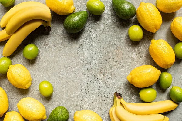 Top view of colorful bananas, avocado, limes and lemons on grey concrete surface with copy space — Stock Photo