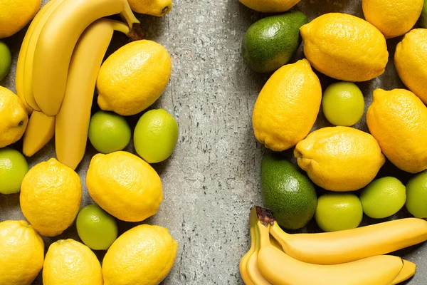 Вид сверху на красочные бананы, авокадо, лаймы и лимоны на серой бетонной поверхности — стоковое фото