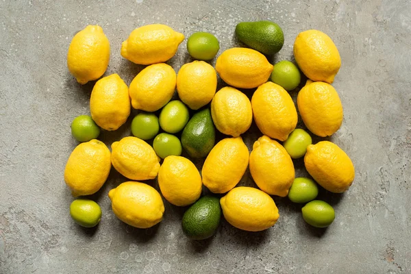 Vue de dessus de l'avocat coloré, des citrons verts et des citrons sur la surface en béton gris — Photo de stock