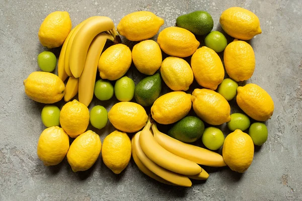 Vista dall'alto di banane colorate, avocado, lime e limoni su una superficie di cemento grigio — Foto stock