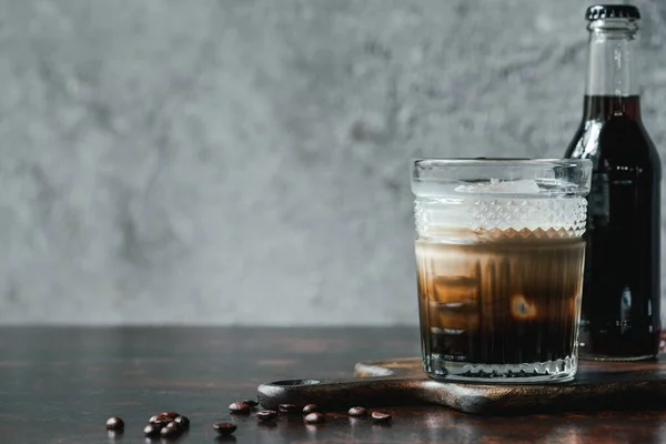 Café infusé à froid avec du lait en verre et bouteille près des grains de café sur une table en bois — Photo de stock