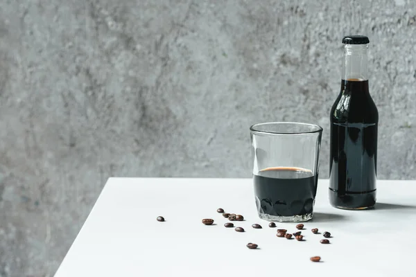 Caffè freddo in vetro e bottiglia vicino ai chicchi di caffè sul tavolo bianco — Foto stock