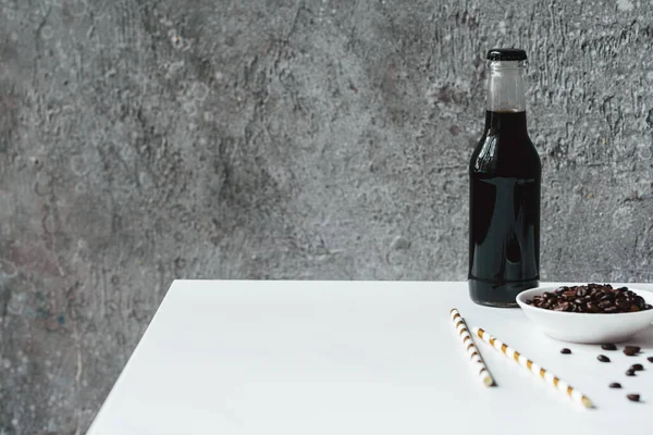 Selektiver Fokus von kaltem Brühkaffee mit Eis in der Flasche in der Nähe von Trinkhalmen und Kaffeebohnen auf weißem Tisch — Stockfoto