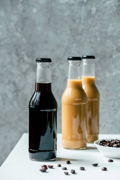 Selektiver Fokus von kaltem Brühkaffee in Flaschen in der Nähe von Kaffeebohnen auf weißem Tisch — Stockfoto