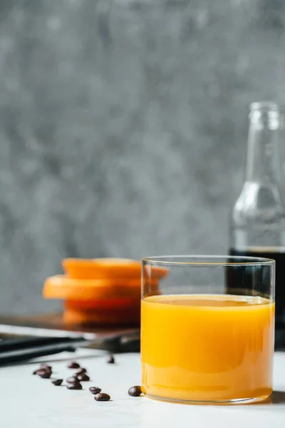 Selective focus of orange juice in glass near cold brew coffee and coffee beans on white table — Stock Photo