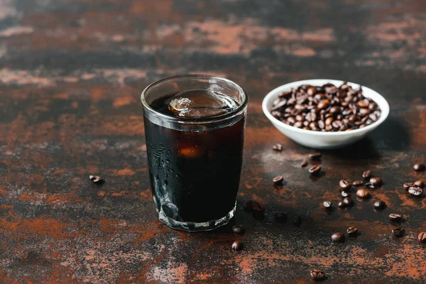 Selektiver Fokus von kaltem Brühkaffee mit Eis im Glas in der Nähe von Kaffeebohnen auf rostiger Oberfläche — Stockfoto