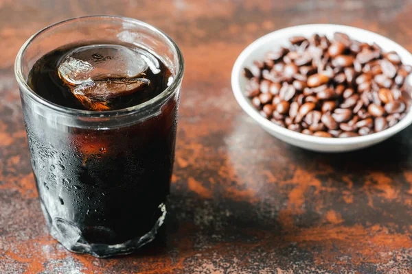 Selective focus of cold brew coffee with ice in glass and bottle near coffee beans on rusty surface — Stock Photo