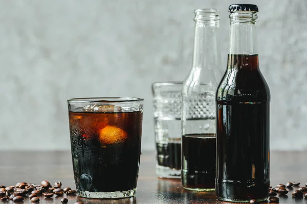 Selective focus of cold brew coffee with ice in glass and bottles near coffee beans — Stock Photo