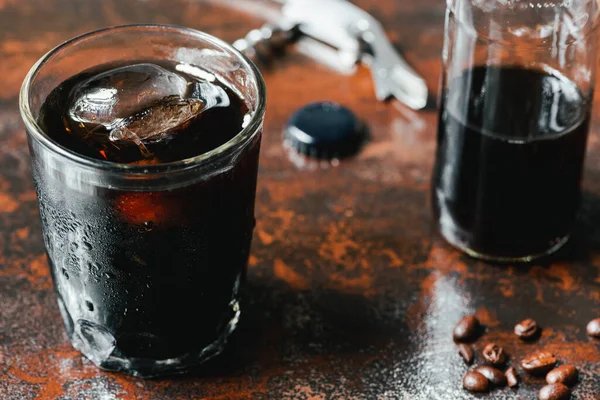 Selective focus of cold brew coffee with ice in glass and bottle near coffee beans on rusty surface — Stock Photo