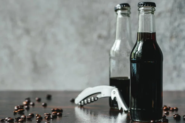 Selective focus of cold brew coffee in bottles near opener and coffee beans — Stock Photo