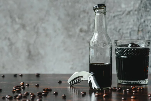 Холодный кофе в стакане и бутылке возле открывашки и кофейных зерен — стоковое фото