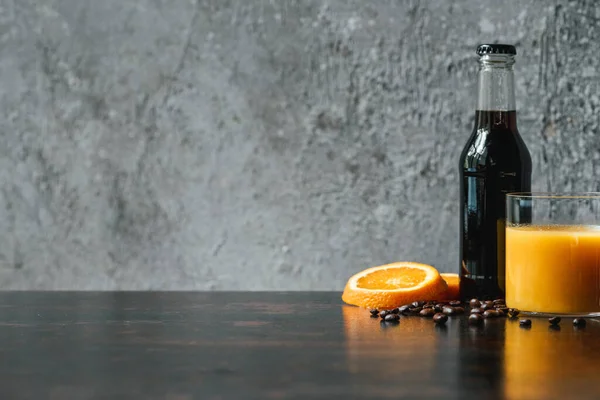 Селективний фокус холодної кави в пляшці біля апельсинового соку та кавових зерен — стокове фото