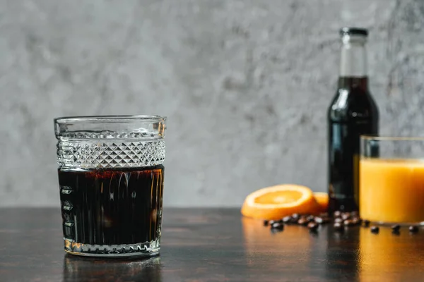 Селективное внимание холодного кофе возле бутылки, апельсинового сока и кофейных зерен — стоковое фото