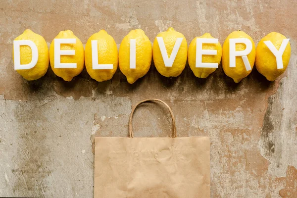 Top view of word delivery on lemons near paper bag on weathered surface — Stock Photo