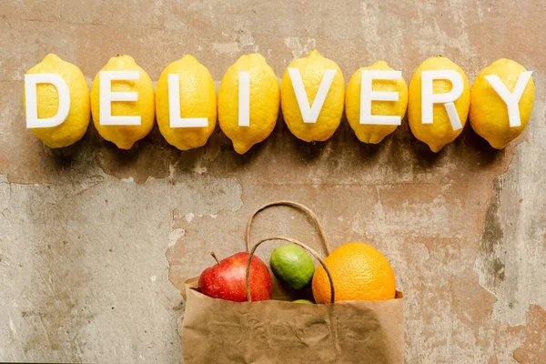 Top view of word delivery on lemons near paper bag with fruits on weathered surface — Stock Photo