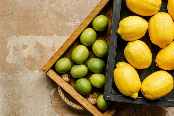 Vue de dessus des citrons et des citrons verts dans des boîtes en bois sur la surface altérée — Photo de stock