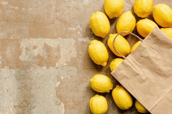 Vista superior de limones y bolsa de papel en superficie erosionada - foto de stock