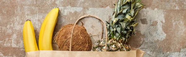 Vista dall'alto di frutta fresca tropicale in sacchetto di carta su superficie intemperie, coltura panoramica — Foto stock