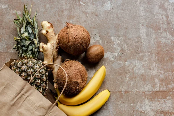 Top view of tropical fresh fruits and ginger root in paper bag on weathered surface — Stock Photo
