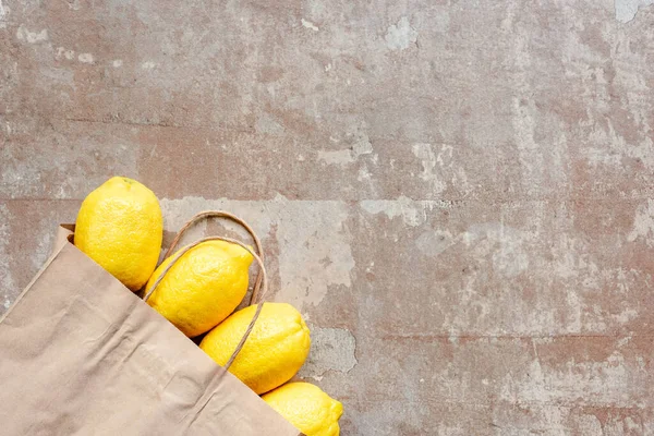 Top view of paper bag with yellow lemons on weathered beige surface — Stock Photo