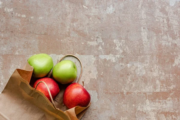 Vista superior de la bolsa de papel con manzanas rojas y verdes en la superficie beige envejecida - foto de stock